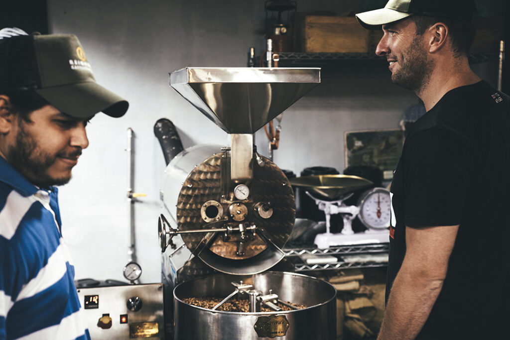 Kaffeeröster und Farmer stehen gemeinsam an einer Röstmaschine und tauschen sich aus