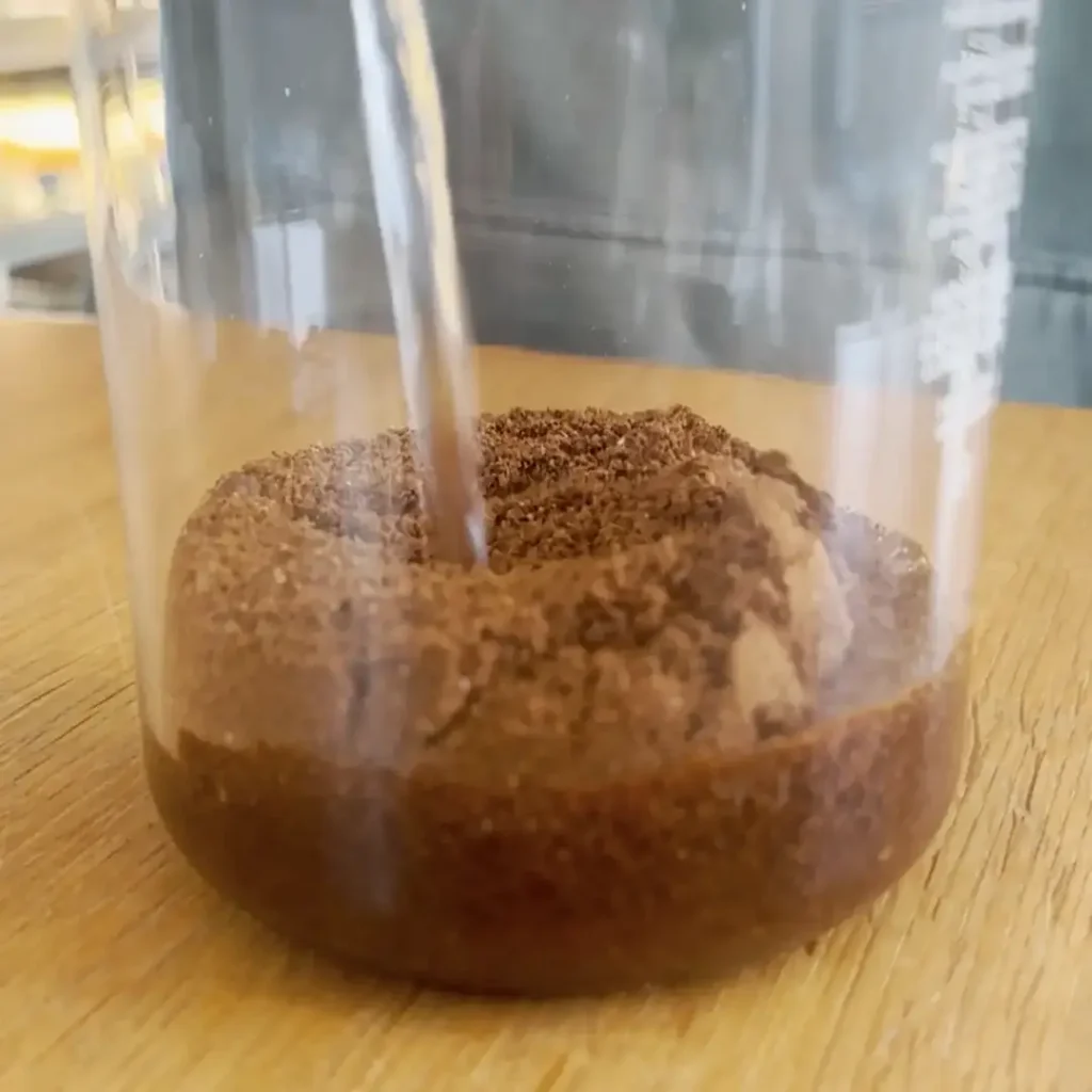 Grob gemahlener Kaffee wird für Cold Brew mit kaltem Wasser in einem Glasgefäß vermischt.