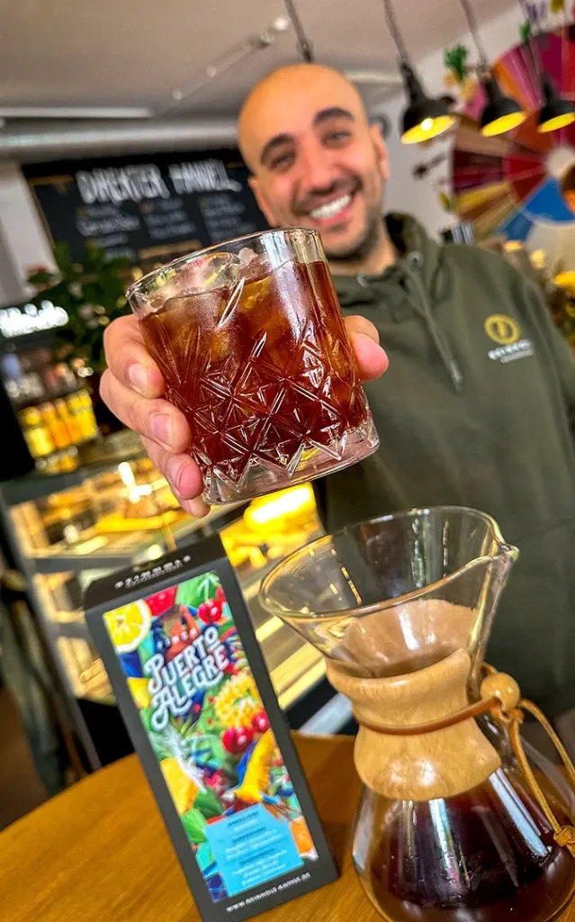 Barista Anton serviert einen frisch zubereiteten Cold Brew auf Eis mit dem Specialty Coffee Puerto Alegre von Reinholz.