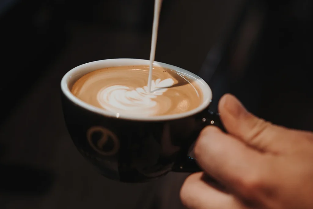 Barista gießt Latte Art auf einen Cappuccino im Reinholz Café am Buttermarkt in Fulda.