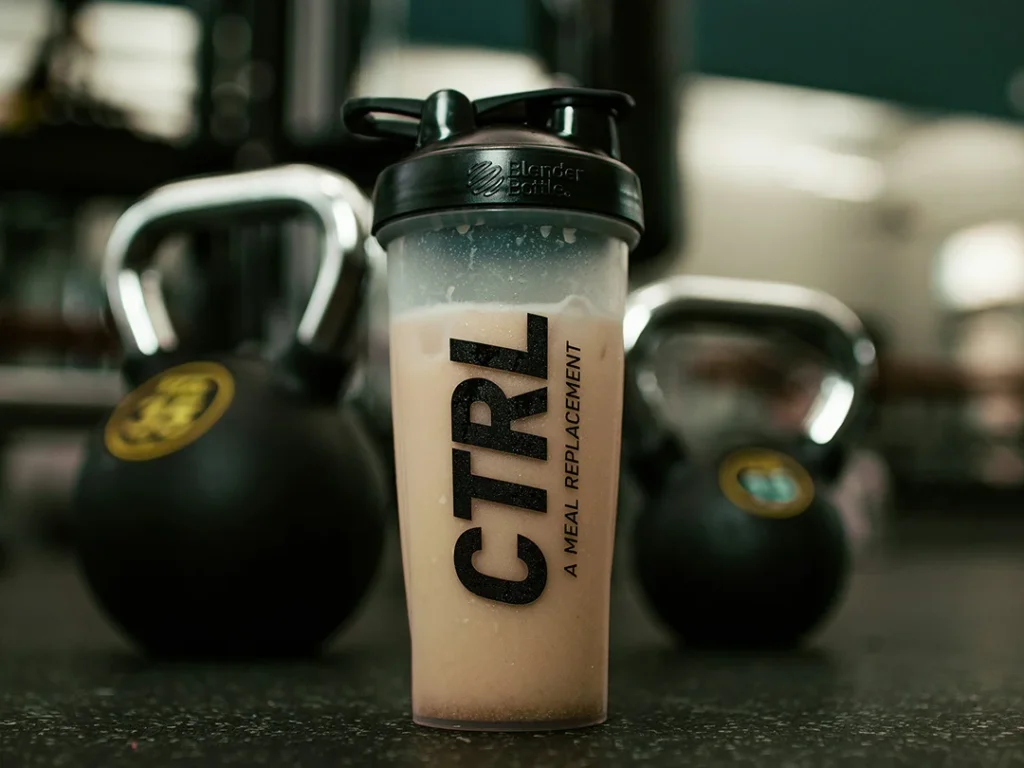 Proteinshake im Shaker vor Kettlebells im Fitnessstudio als Beispiel für den Functional-Coffee-Trend 2026
