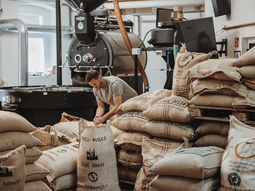 Röstmeister Heiko zwischen Rohkaffeesäcken vor dem Trommelröster in der Reinholz Kaffeerösterei in Fulda-Bronnzell.